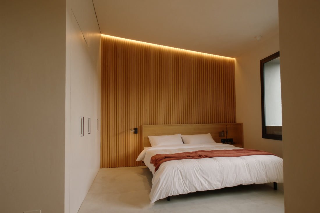 Quarto com parede de ripado atrás da cama e luz linear quente.